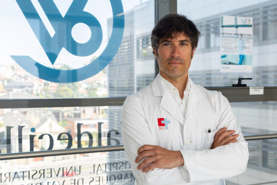 Dr. Mario Domínguez Esteban, in a white coat with his arms crossed, in front of the glass frontage of Hospital Universitario Marqués de Valdecilla