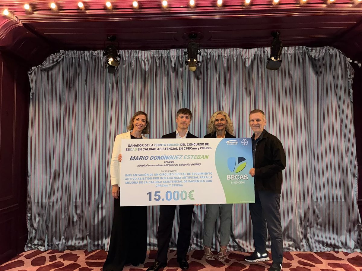 Mario Domínguez Esteban, con otras tres personas, sostiene el cheque simbólico de la 5.ª edición de las Becas en Calidad Asistencial en cáncer de próstata, con los logotipos de Orion Pharma y Bayer